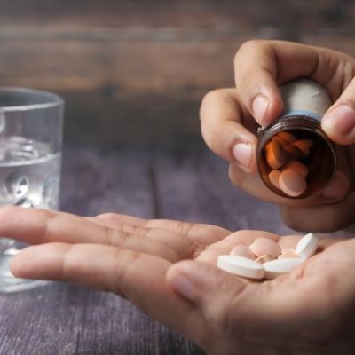 A closeup image of a hand tipping tablet medication into an open palm. There is a glass of water in the background. 